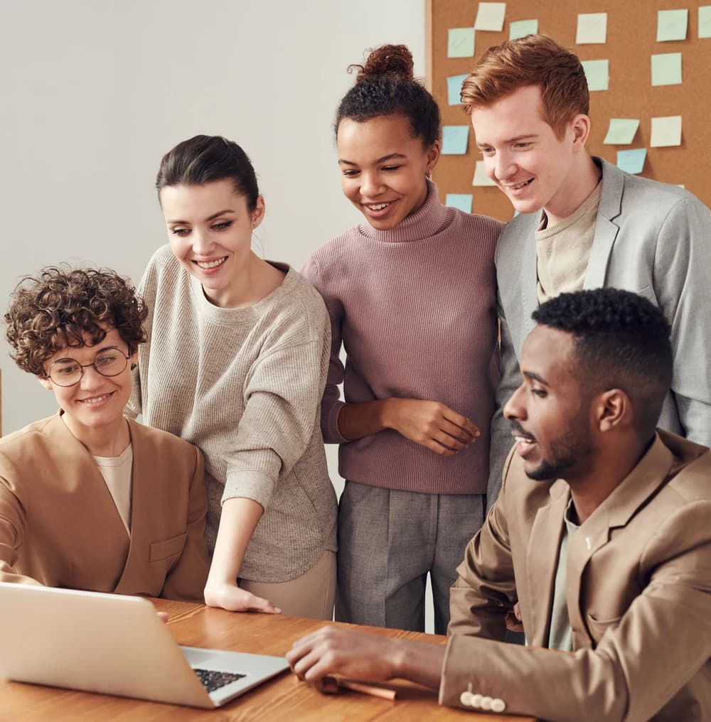 A team of five gathered around a laptop, reviewing work together