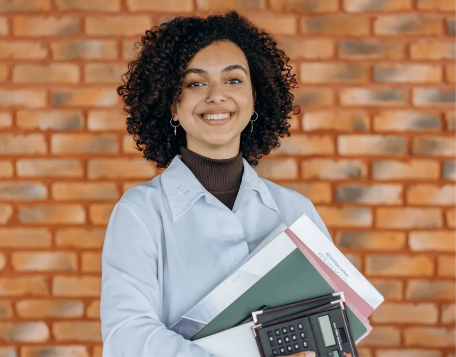 Bookkeeper holding folders and a calculator in front of a brick wall